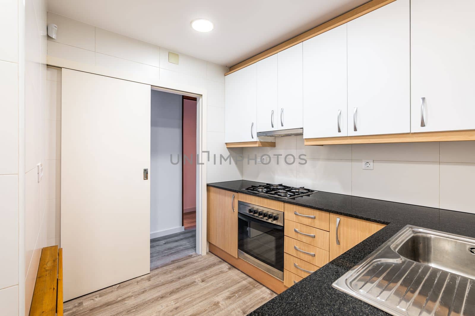 Modular furniture in kitchen with white cabinets on top of wall and cabinets with wood doors below. Black worktop with gas stove. On wall opposite, there is folding solid wood tabletop to save space