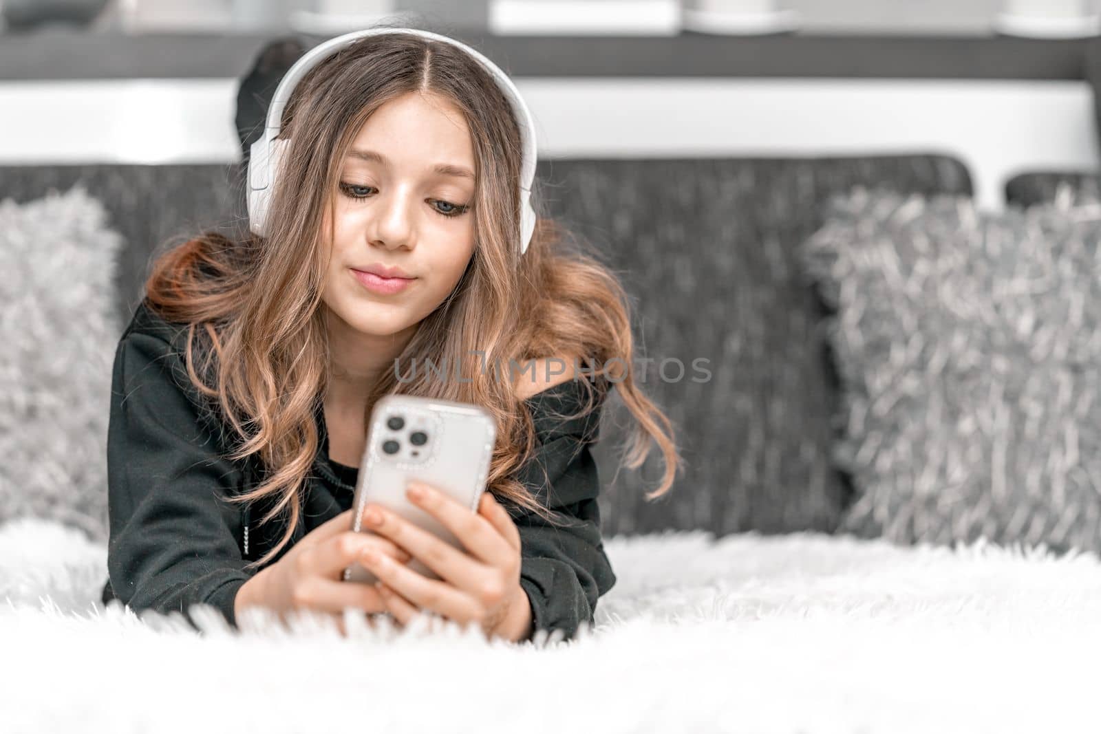 teenager with headphones on head and phone in hand on couch by Edophoto