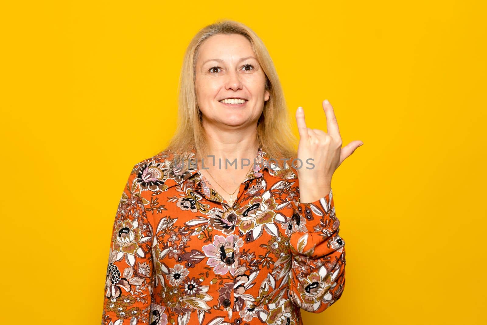 Caucasian blonde woman in her 40s in printed dress doing isolated rock geto on yellow studio background