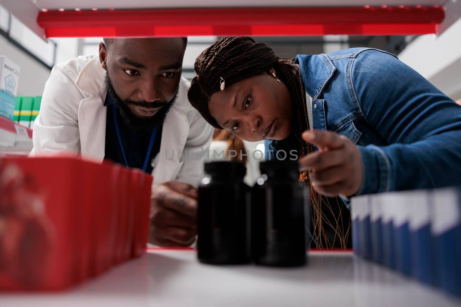 Pharmacist and customer choosing medication on drugstore shelf, close up selective focus. African american woman taking pills packages, pharmaceutical service, medicaments selling