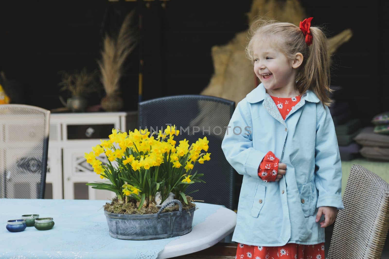 A girl in a dress near a pot of daffodils