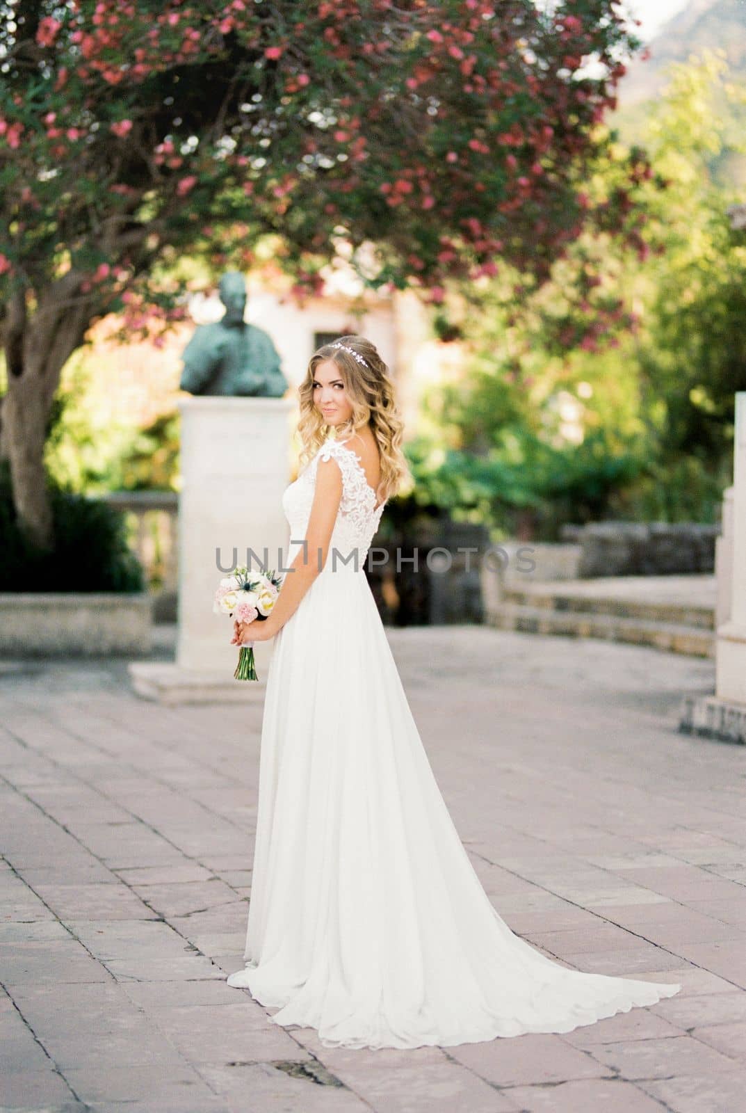 Bride in a white dress with a bouquet stands in the garden against the backdrop of a flowering tree. High quality photo