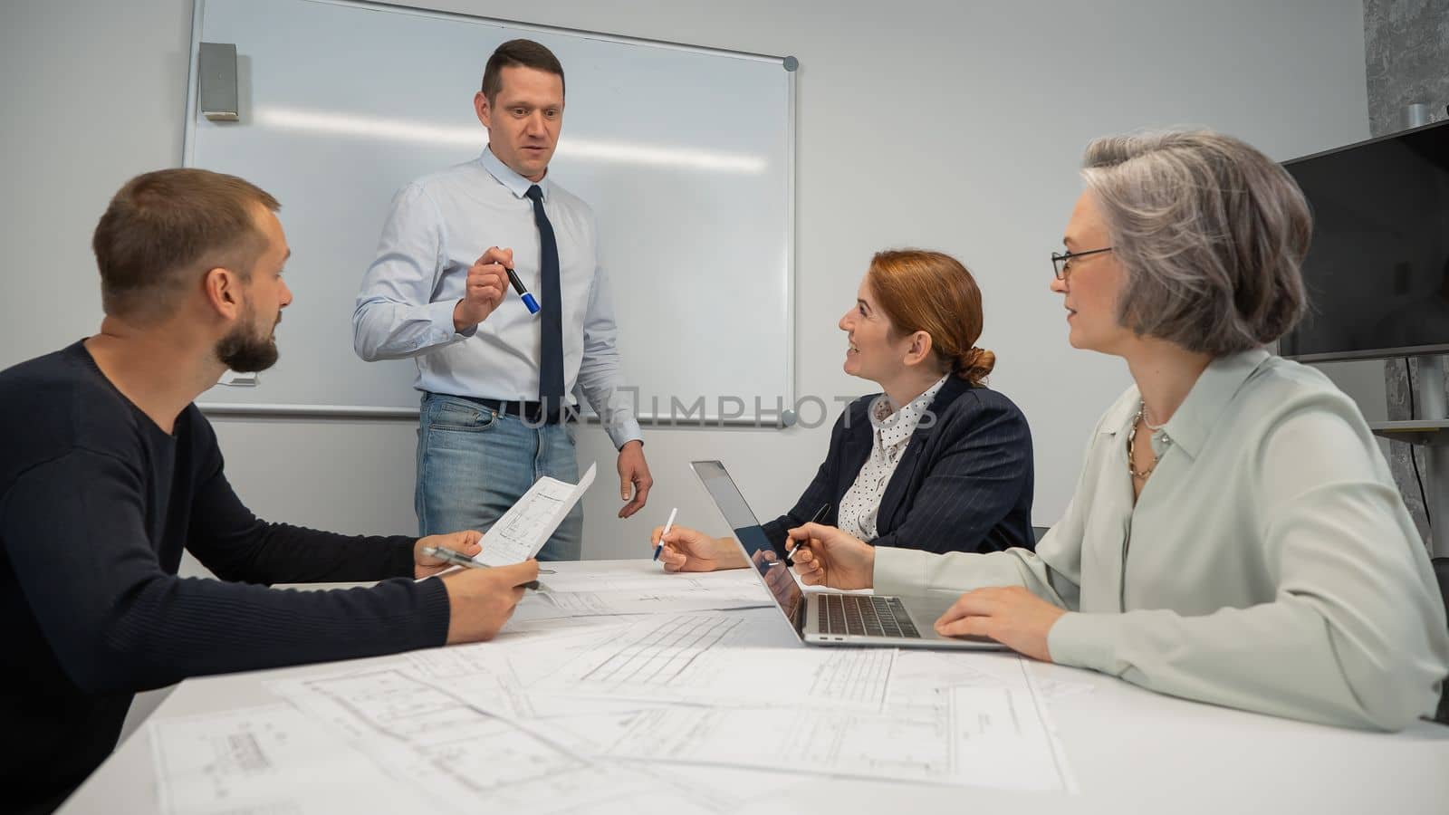 Caucasian man leading a presentation to colleagues at a white board