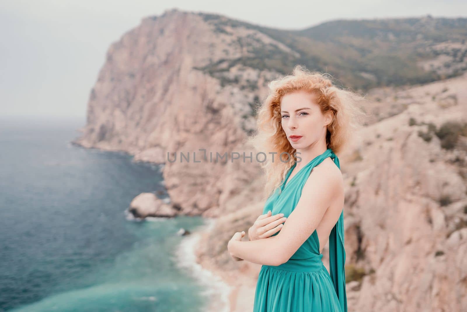 Side view a Young beautiful sensual woman in a mint long dress posing on a volcanic rock high above the sea during sunset. Girl on the nature on overcast sky background. Fashion photo