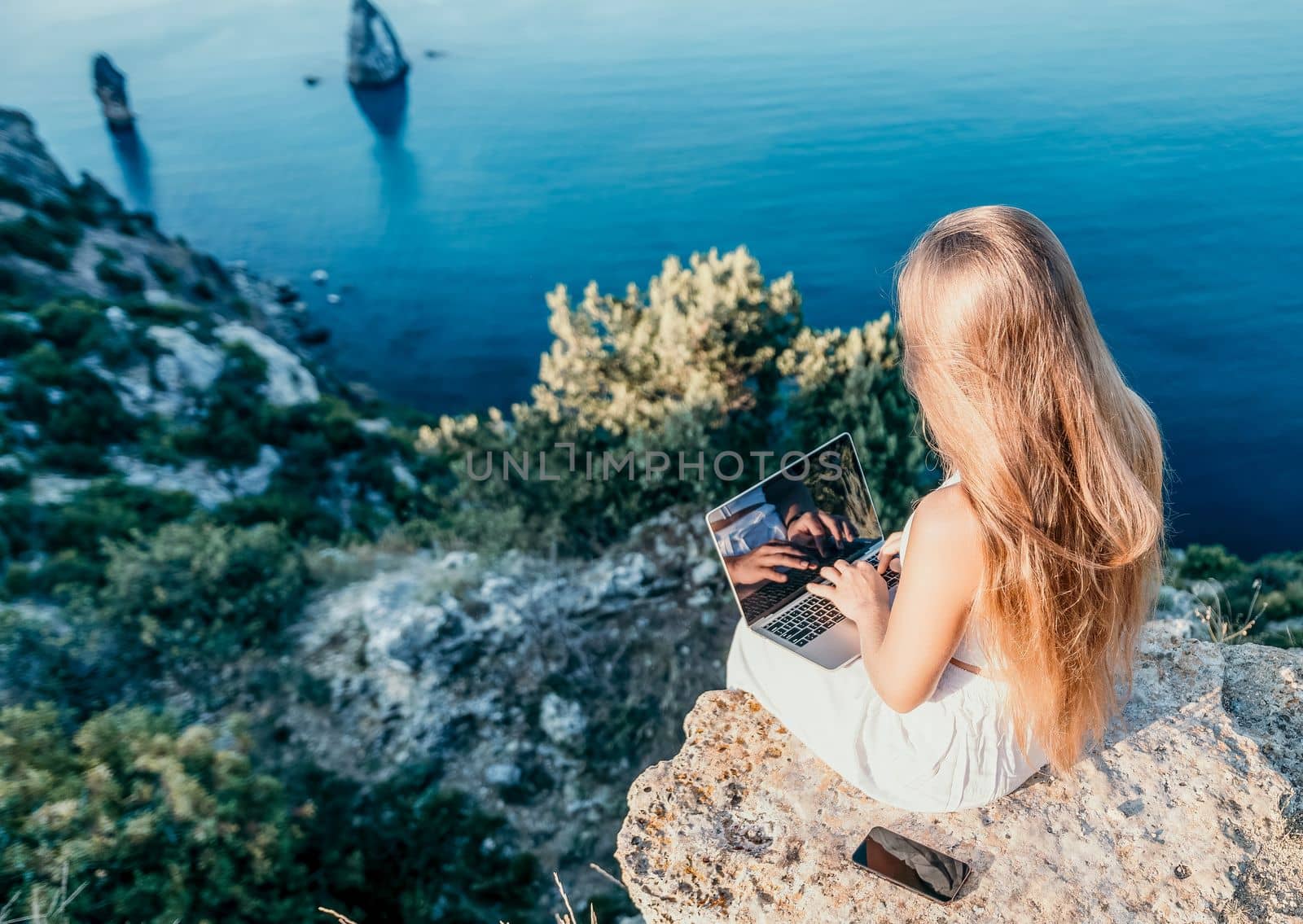 Digital nomad, Business woman working on laptop by the sea. Pretty lady typing on computer by the sea at sunset, makes a business transaction online from a distance. Freelance, remote work on vacation by panophotograph