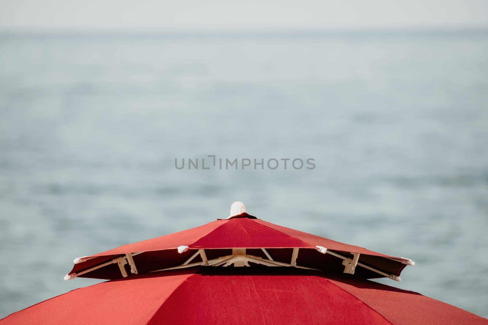 Red Beach Umbrella on the Background of the Blue Sea Ocean. Beach Landscape. Summer travel and holidays concept. by panophotograph
