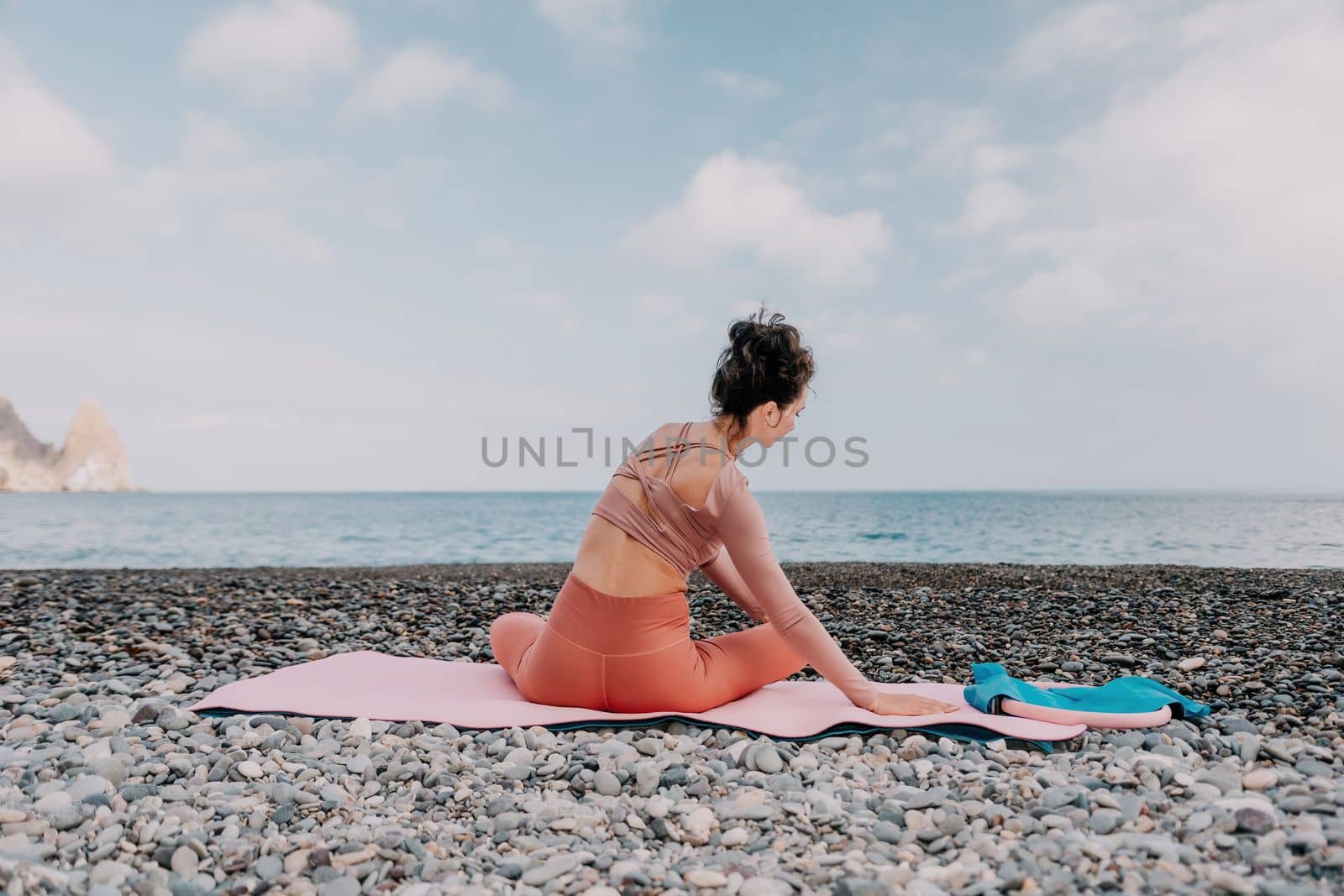 Middle aged well looking woman with black hair doing Pilates with the ring on the yoga mat near the sea on the pebble beach. Female fitness yoga concept. Healthy lifestyle, harmony and meditation.