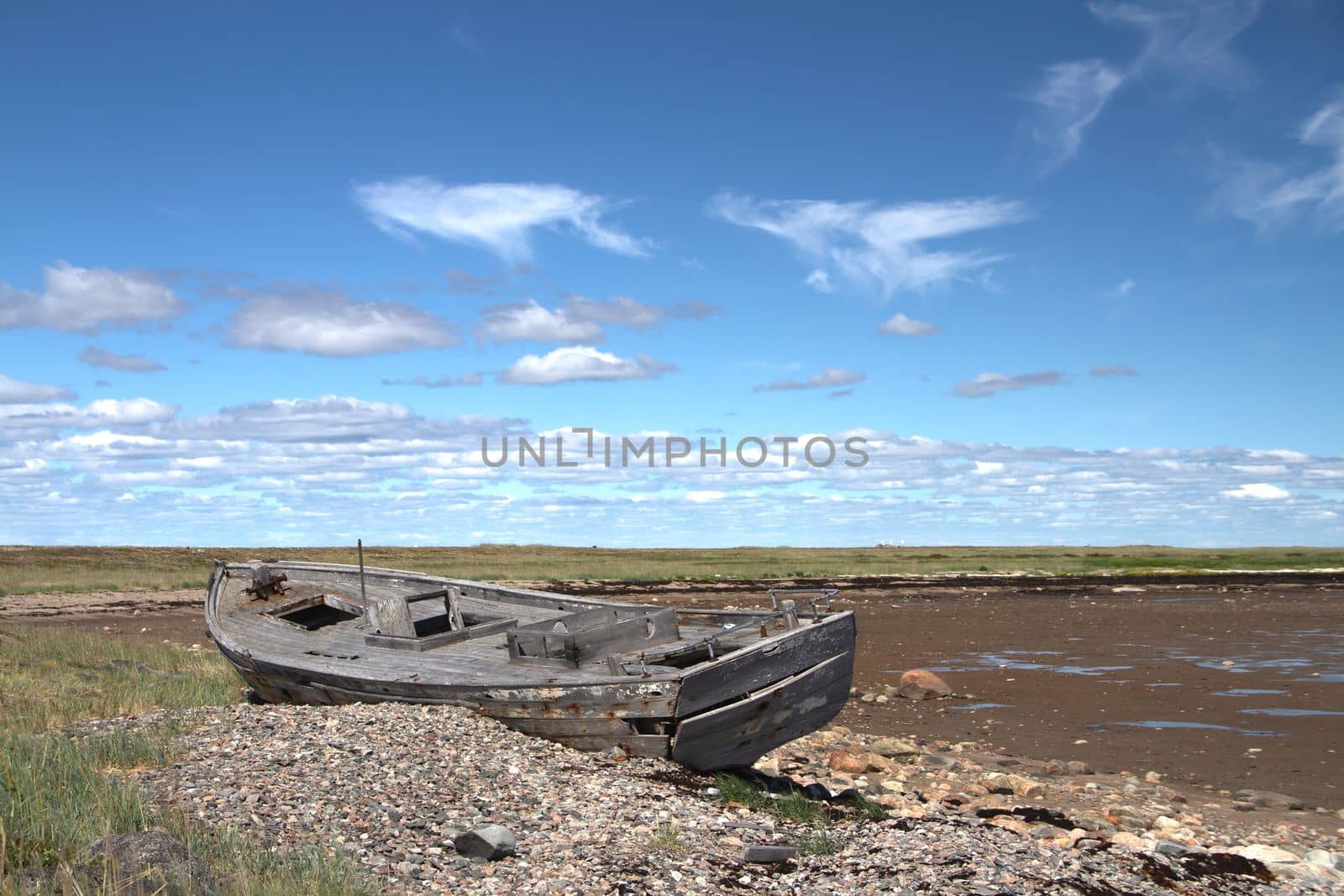 Side view of old wooden boat wrecked and stranded on a rocky shoreline, north of Arviat, Nunavut, Canada