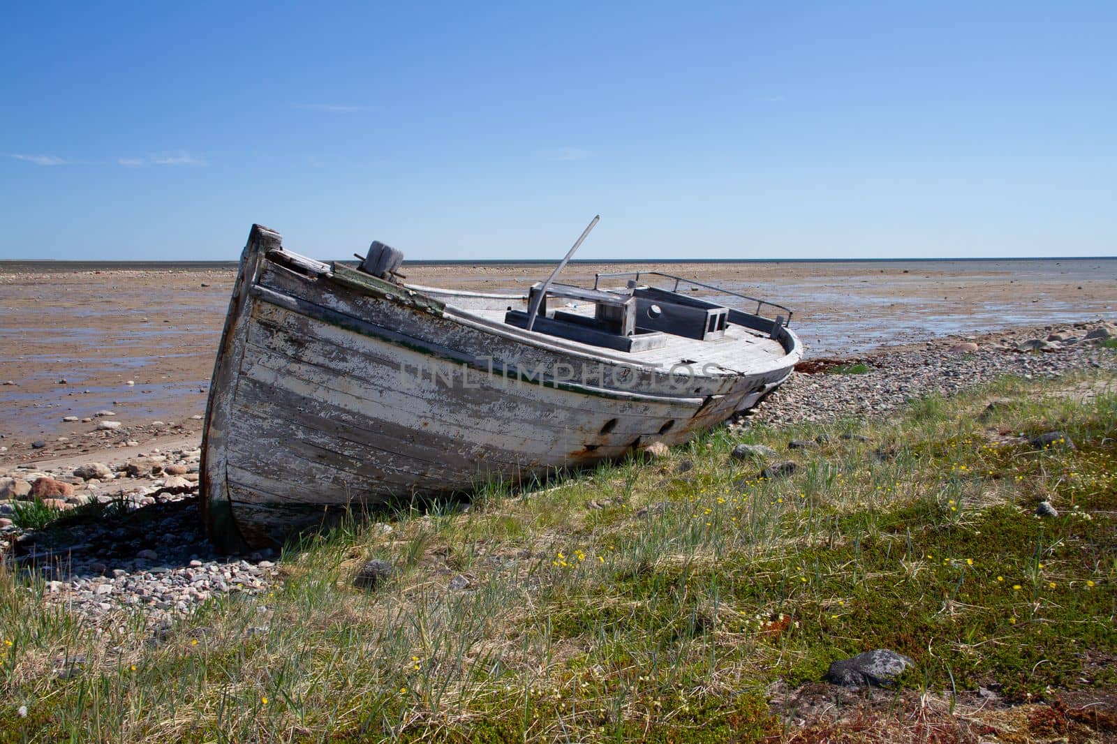 Front view of old wooden boat wrecked and stranded on a rocky shoreline by Granchinho