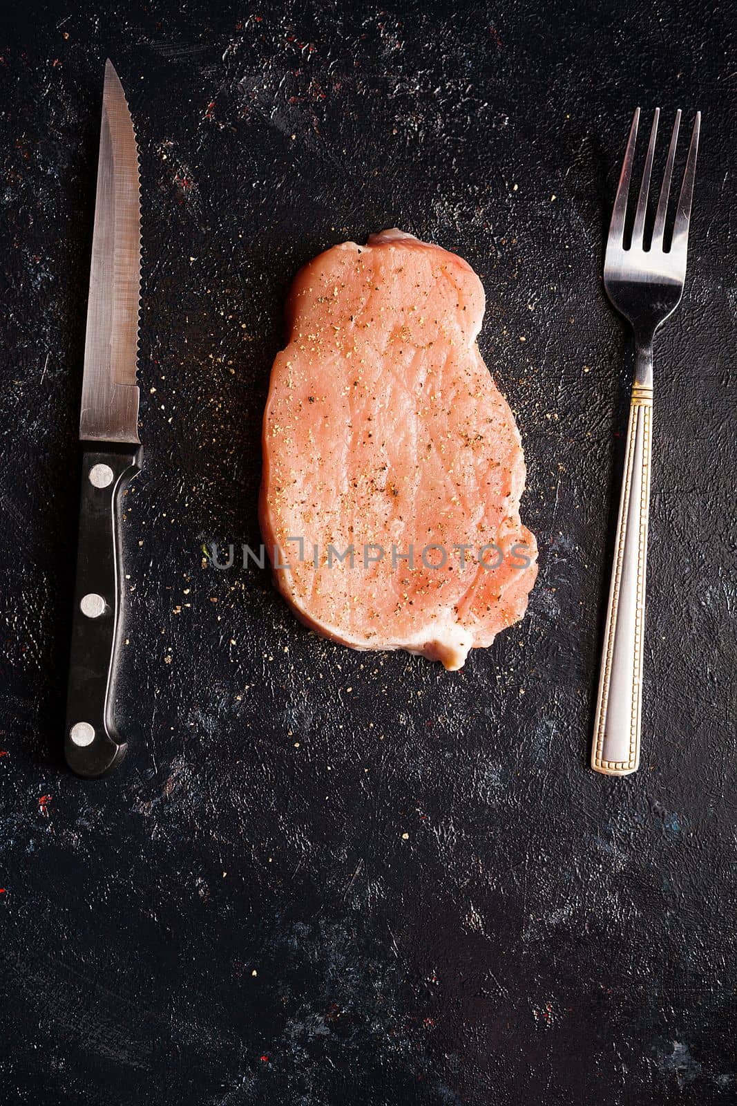 Raw steak meat on black wooden table next to fork and knife by DCStudio