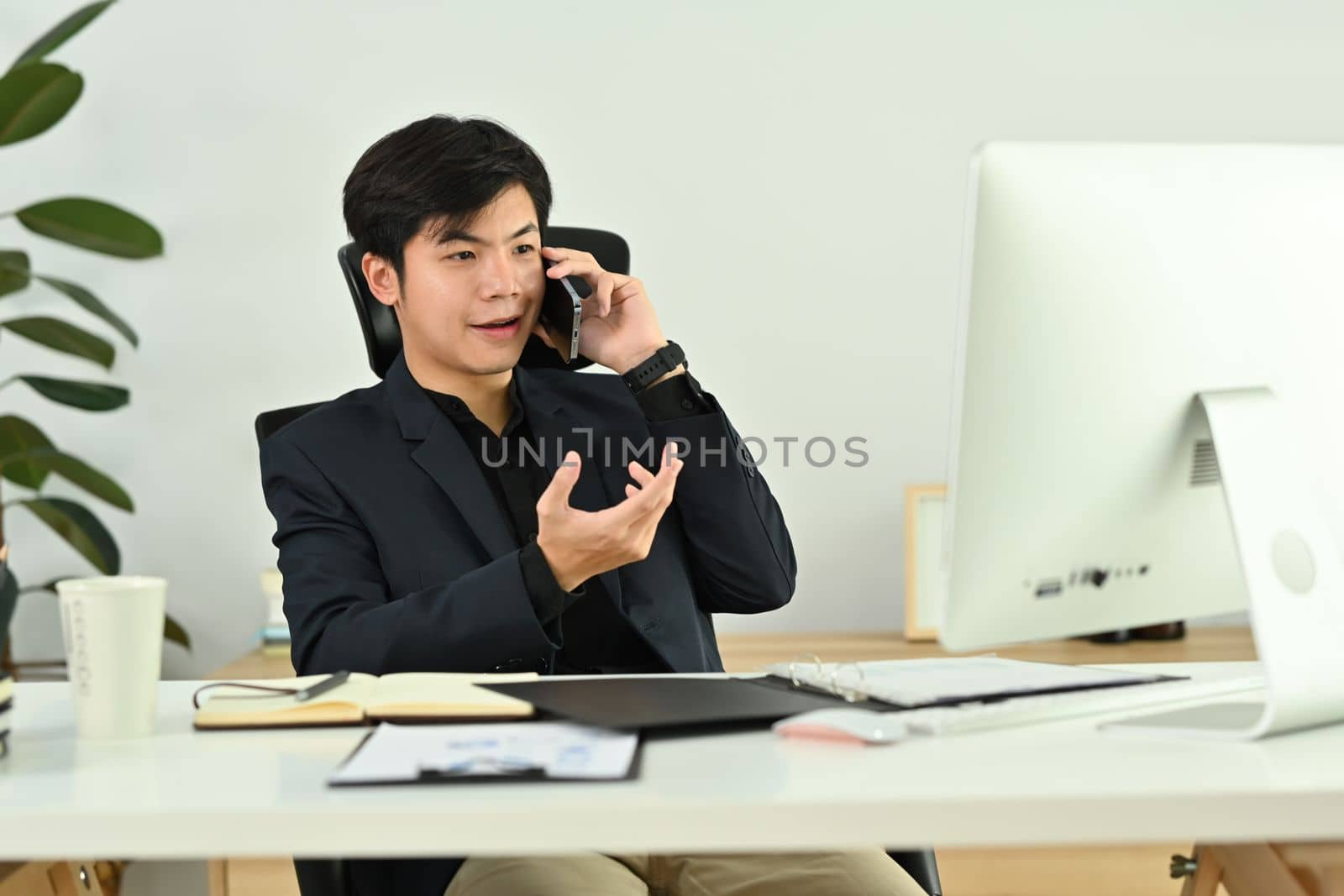 Millennial male business executive looking at laptop computer screen, discussing project on mobile phone by prathanchorruangsak
