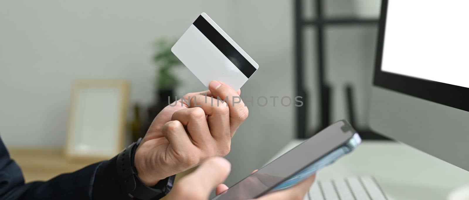 Man holding credit cad and using mobile phone smartphone for online banking transaction or entering data for website form by prathanchorruangsak