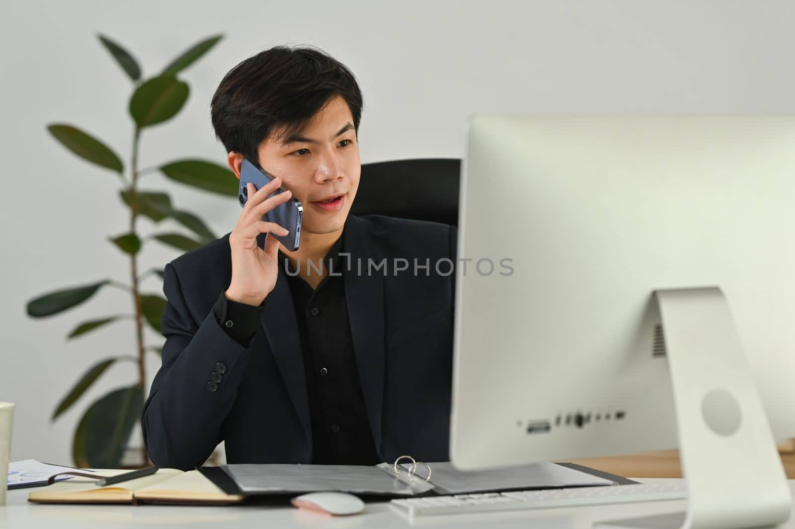 Start up business man making business call, talking on mobile phone and looking at computer monitor.