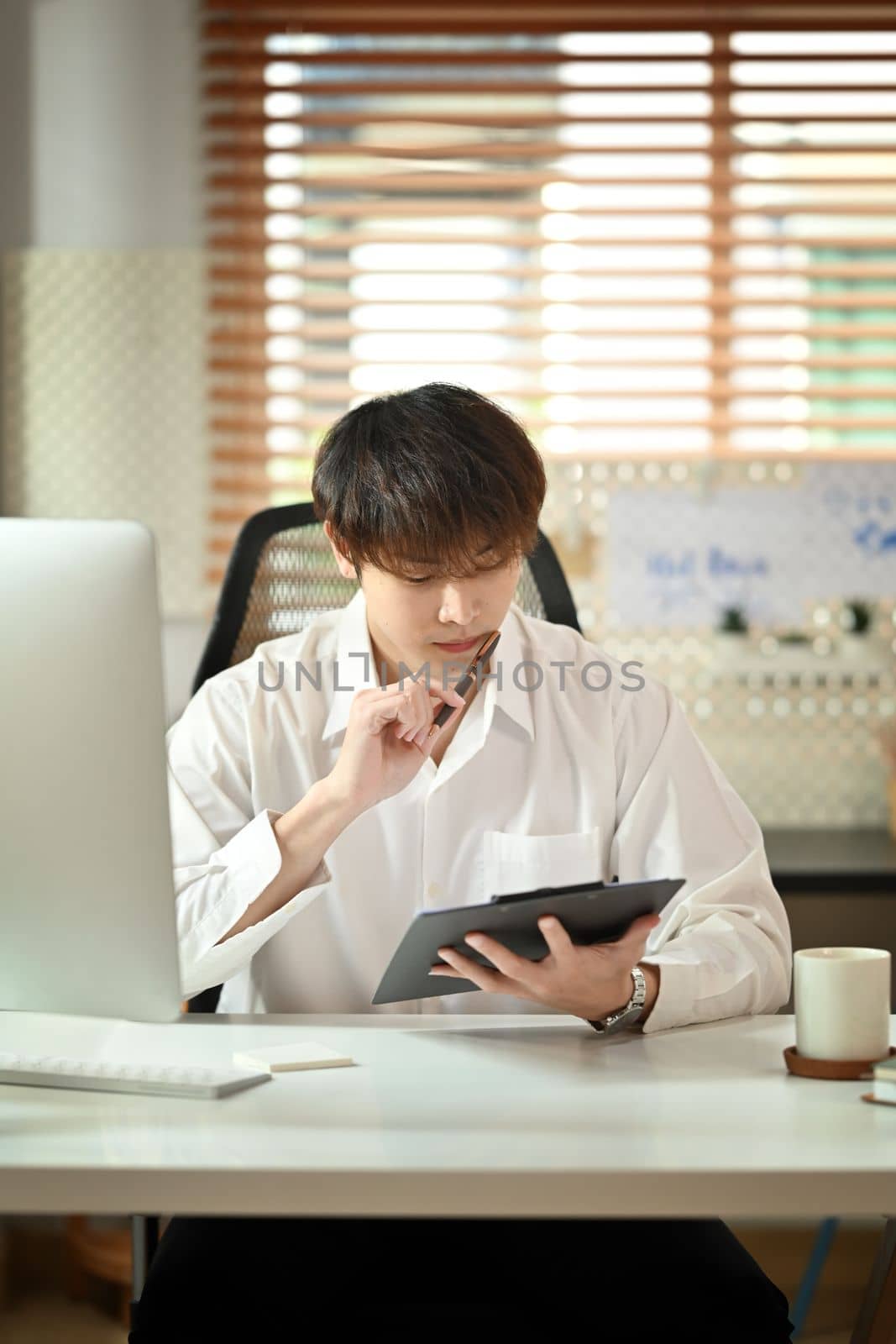 Concentrated male manager in white shirt sitting at working desk and checking financial reports.