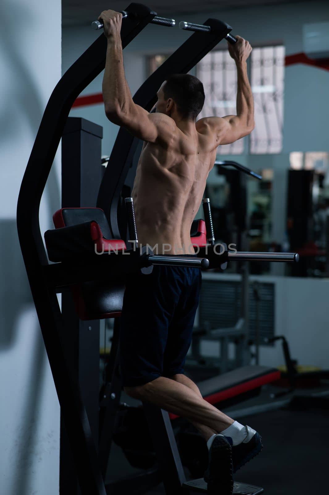 Back view of shirtless man with pull-ups in gym