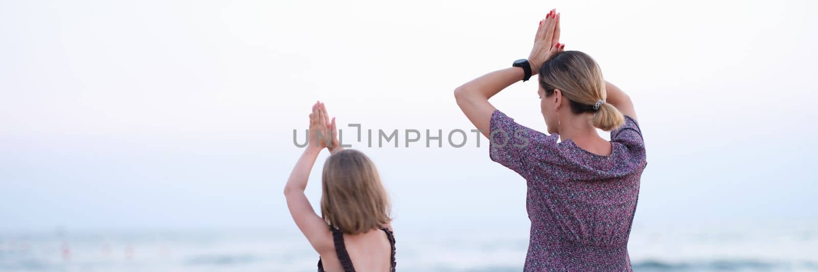 Happy family mother and daughter do yoga, meditate in lotus position on beach by kuprevich