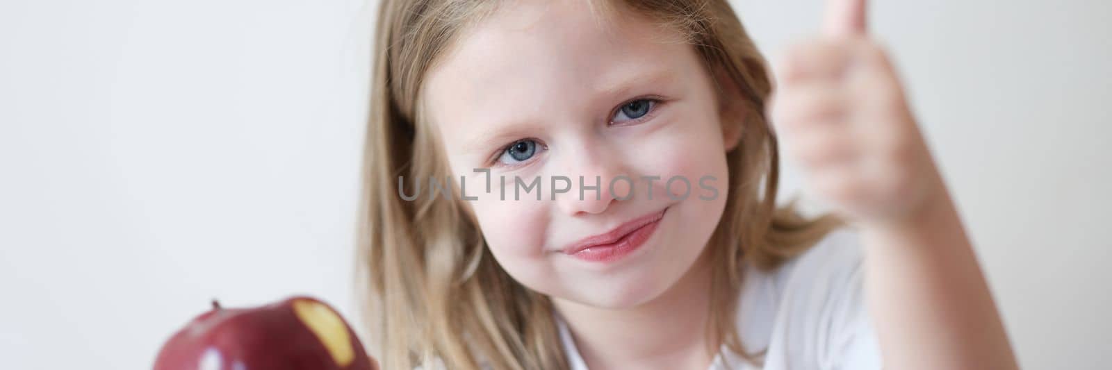 Cute little girl holds apple in one hand and thumbs up. Benefits of apples and fruits for children concept