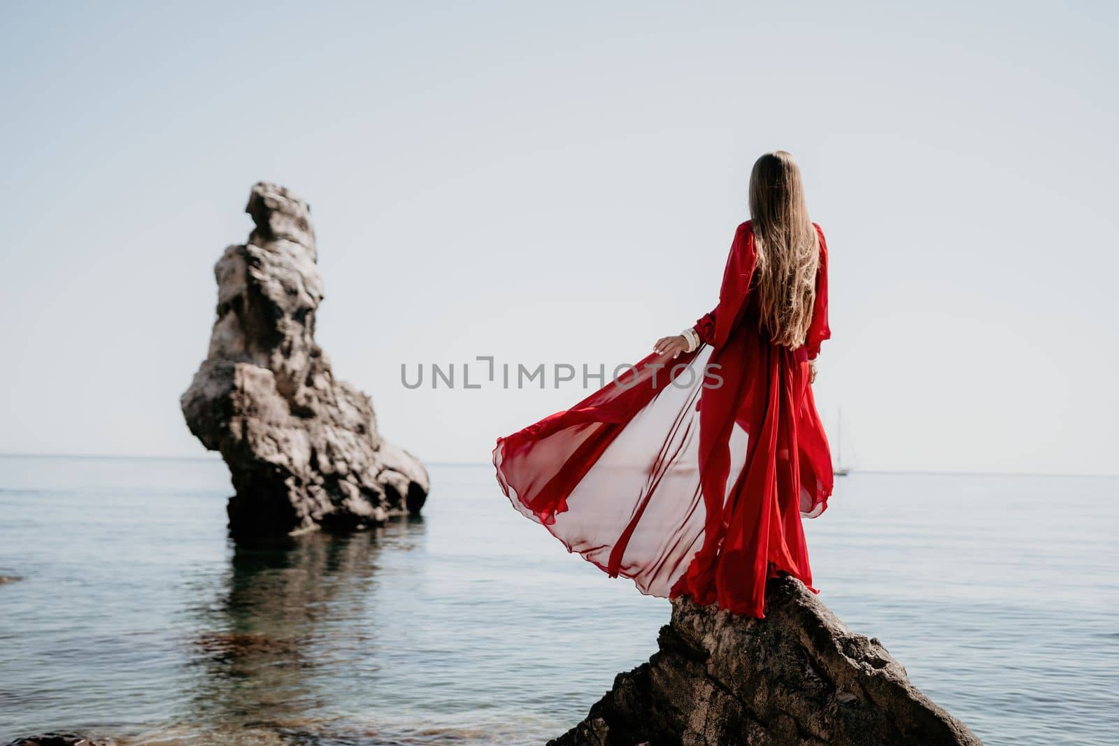 Woman travel sea. Young Happy woman in a long red dress posing on a beach near the sea on background of volcanic rocks, like in Iceland, sharing travel adventure journey by panophotograph