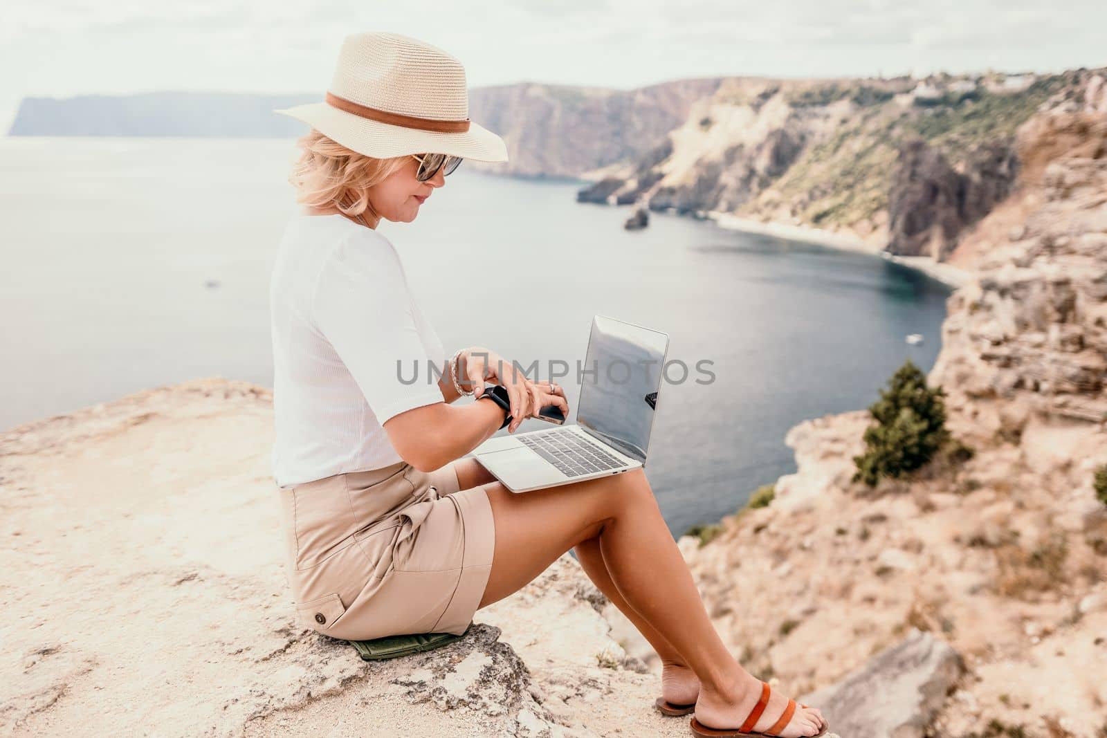 Digital nomad, Business woman working on laptop by the sea. Pretty lady typing on computer by the sea at sunset, makes a business transaction online from a distance. Freelance, remote work on vacation by panophotograph