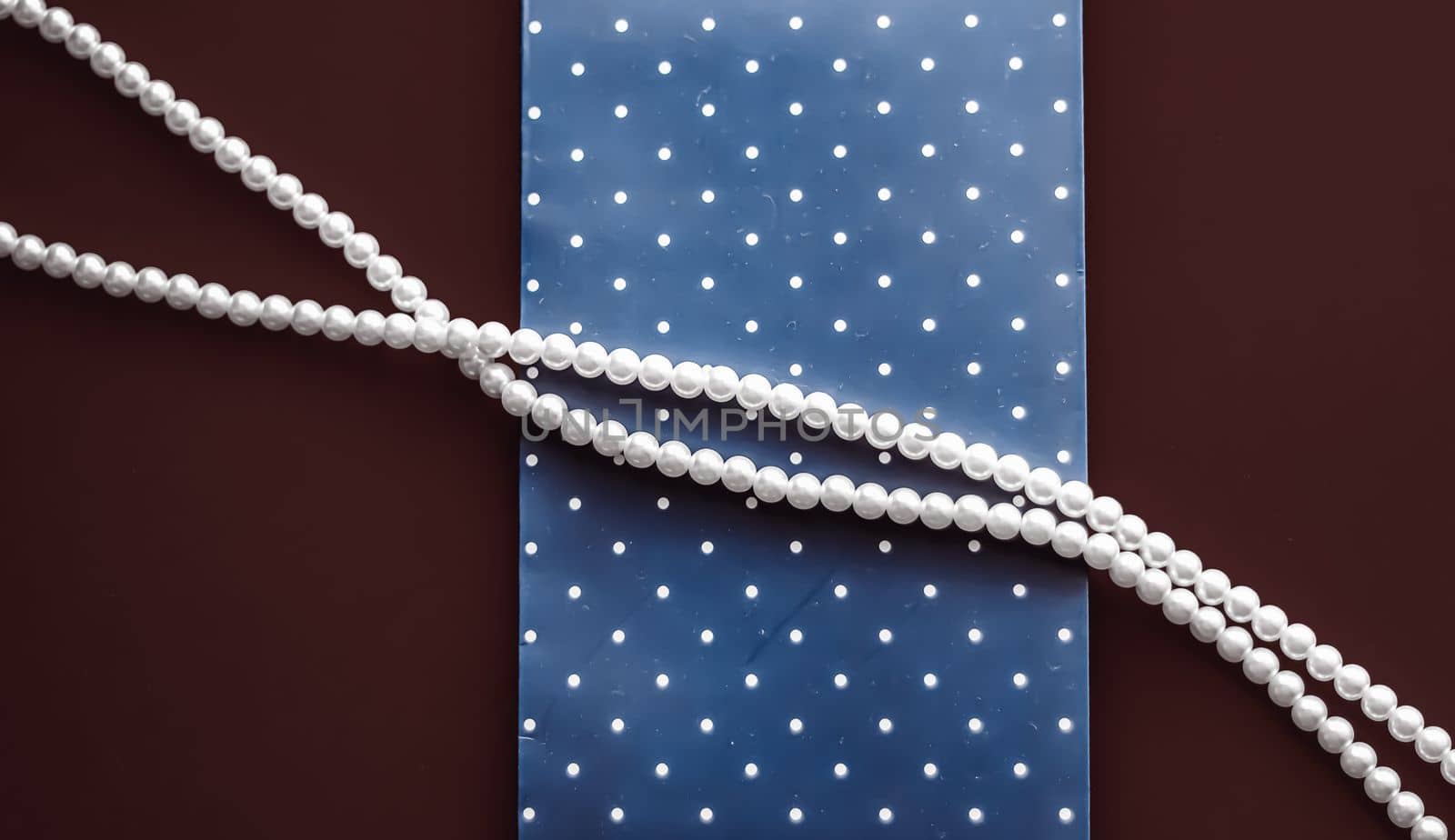 Pearl jewellery necklace and abstract blue polka dot background on chocolate backdrop by Anneleven