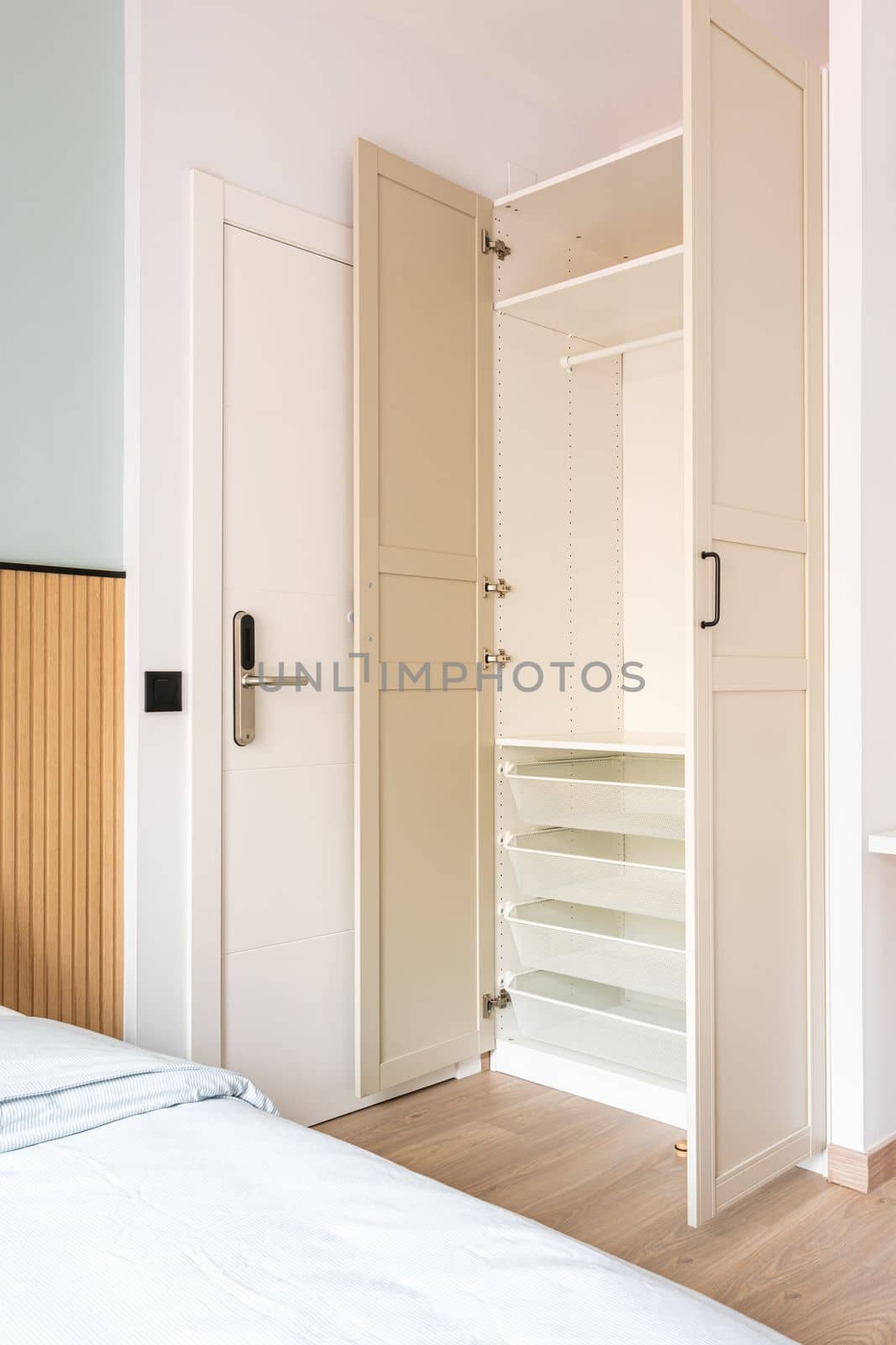 Built-in wooden wardrobe with open doors in beige. Inside the cabinet, all shelves, drawers, crossbars are made of white durable plastic. Entrance to the hotel room with an electronic lock