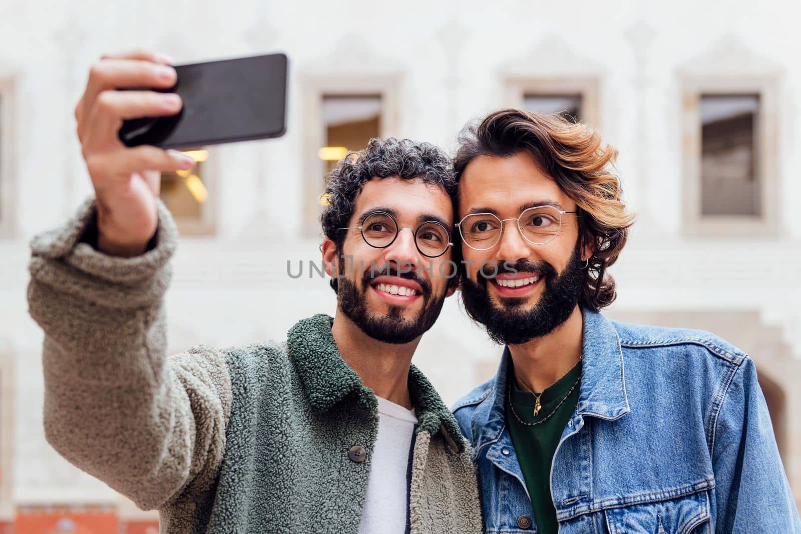 gay male couple taking a selfie photo with their mobile phone in the street, concept of urban lifestyle and love between people of the same sex