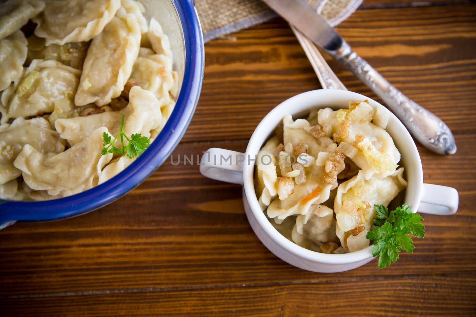 cooked dumplings with potatoes and fried onions, in a bowl on a wooden table.