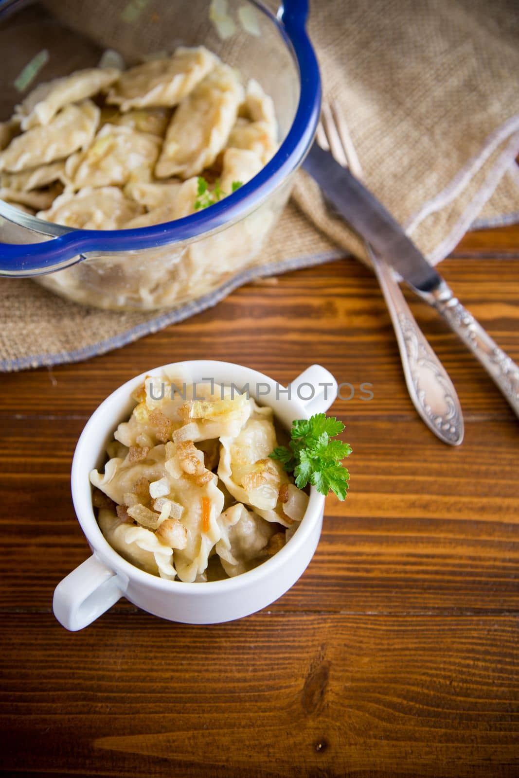 cooked dumplings with potatoes and fried onions, in a bowl on a wooden table.