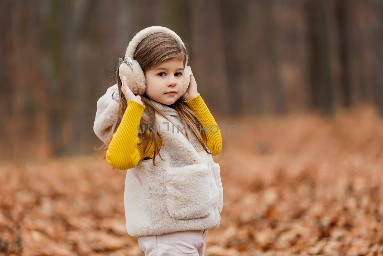 little girl in headphones walks through the autumn forest