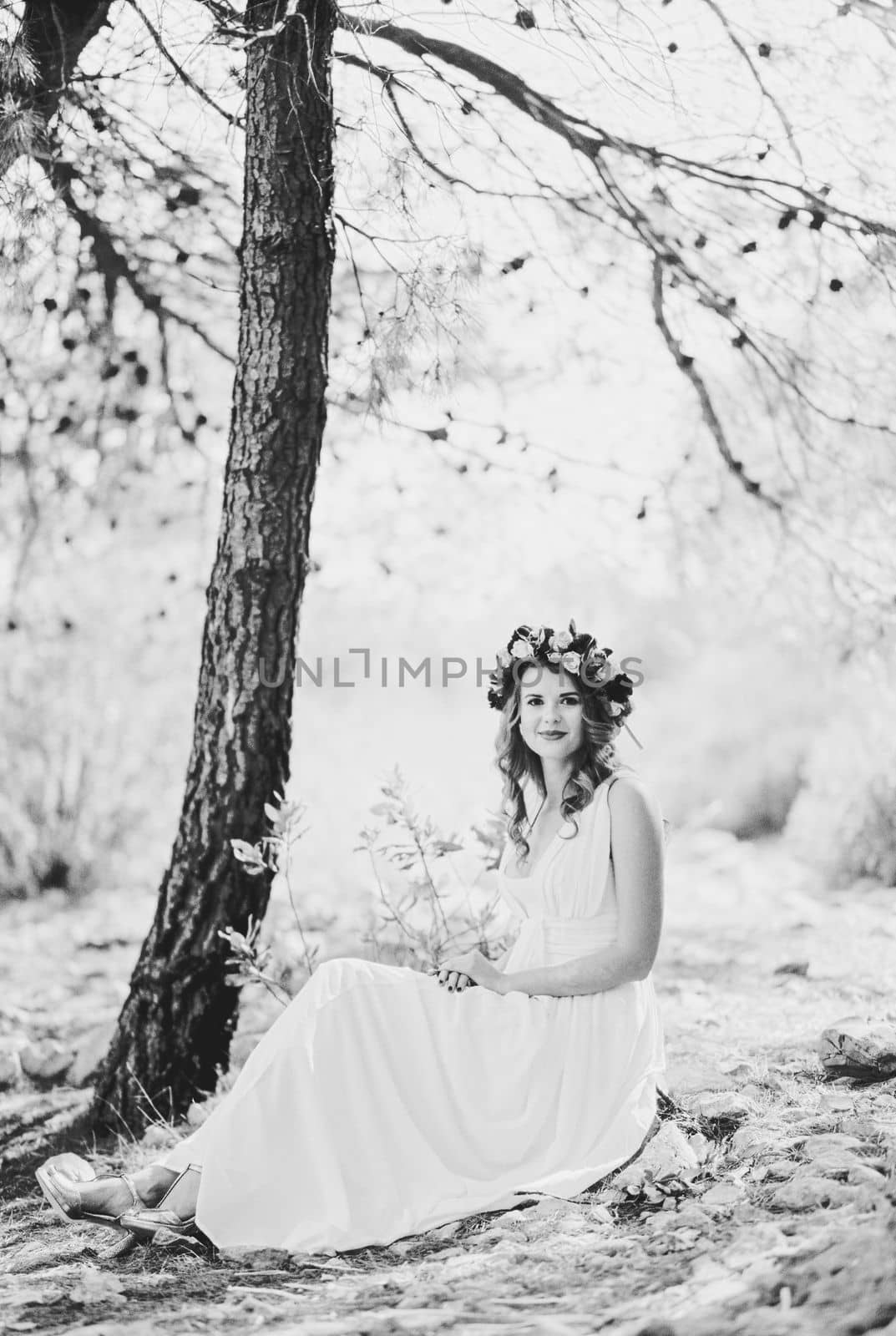 Bride in a wreath on her head sits under a tree. Black and white photo. High quality photo
