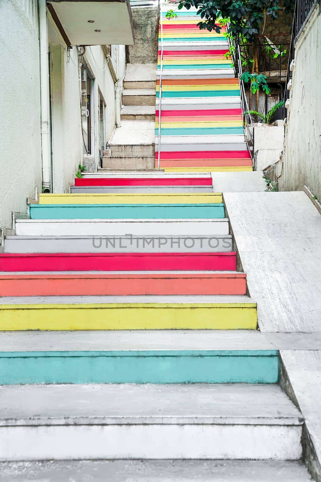 Stairs are painted with multicolored paint, rising up narrow street, view from below, concept of positivity