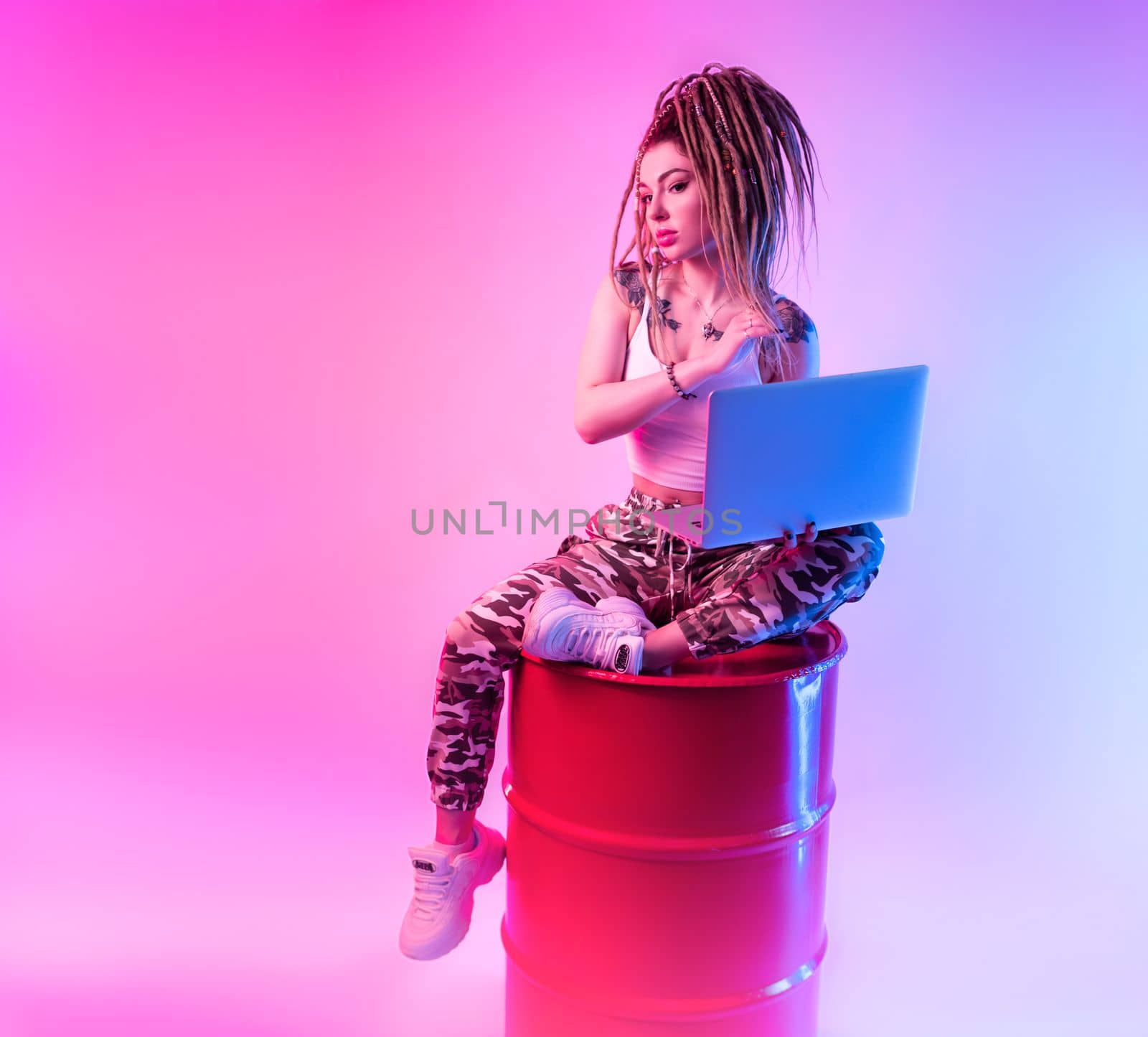 sexy girl with braids dreadlocks on her head in neon light with a laptop on a light background copy paste