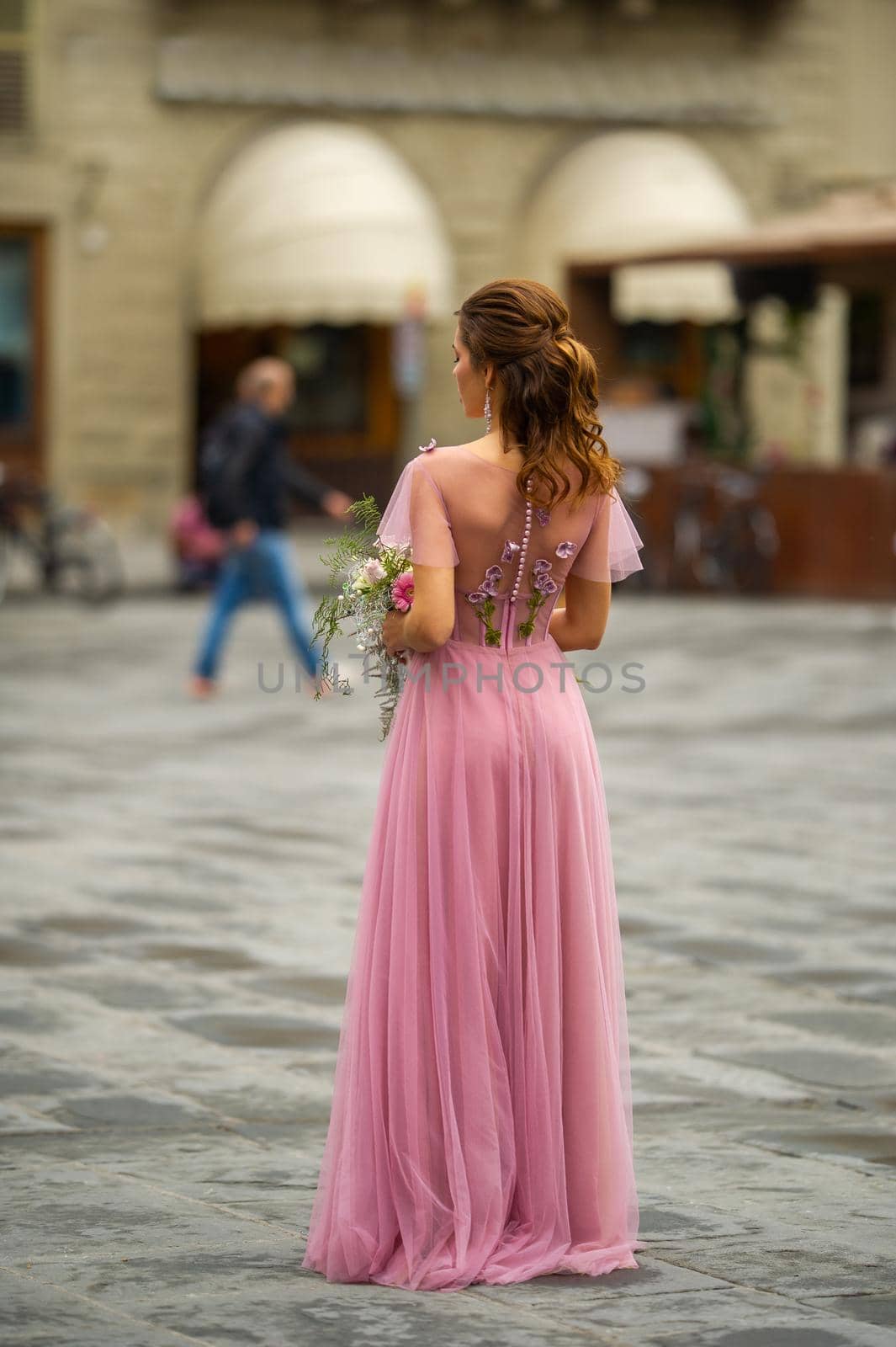 A bride in a pink dress with a bouquet stands in the center of the Old City of Florence in Italy.