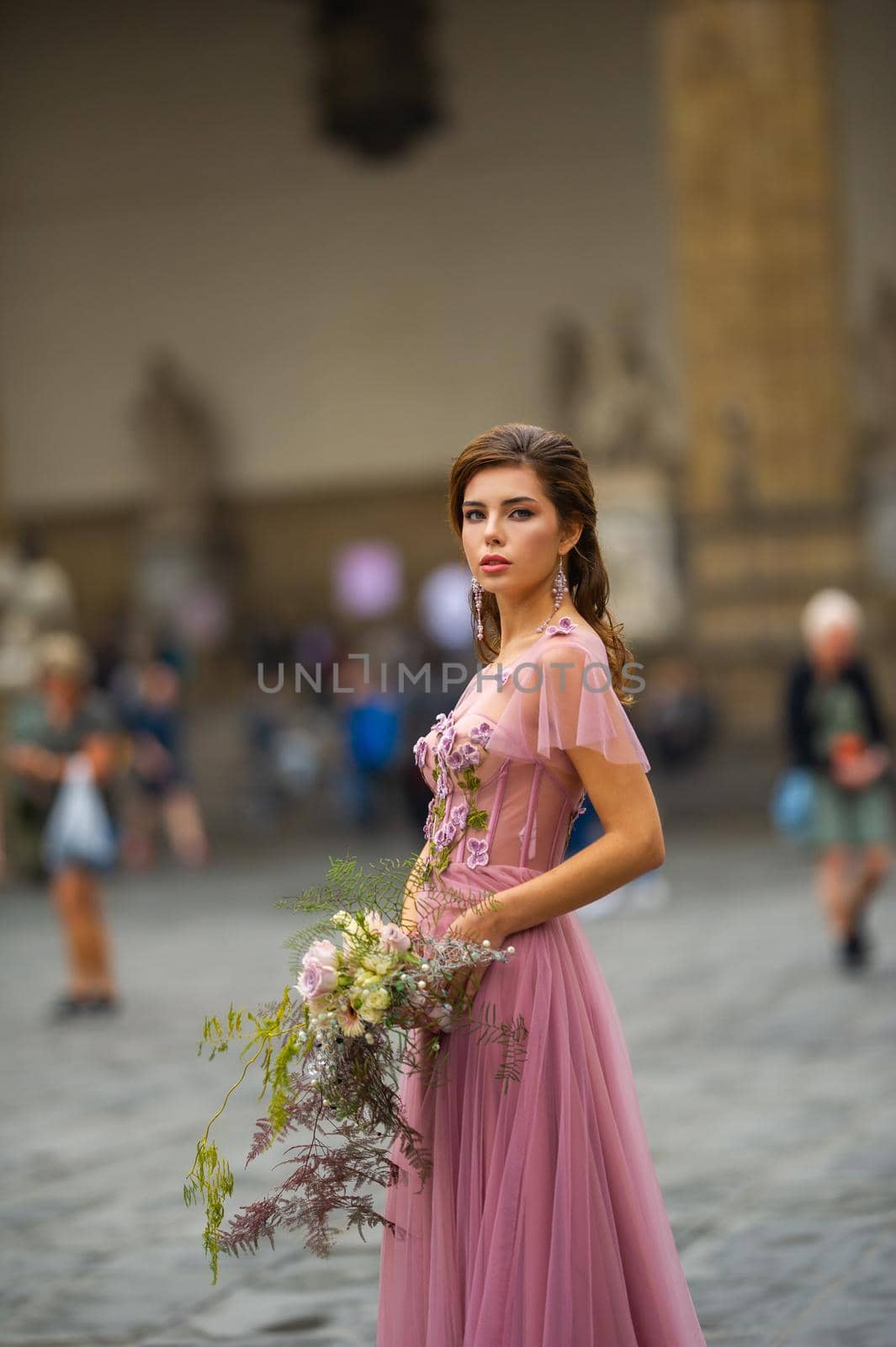 A bride in a pink dress with a bouquet stands in the center of the Old City of Florence in Italy by Lobachad