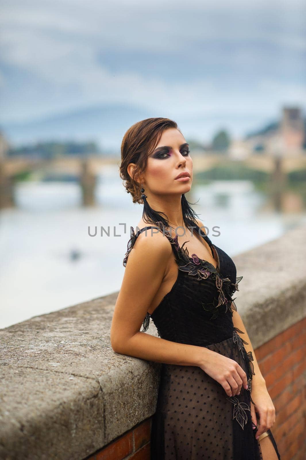 Beautiful stylish bride in a black dress stands on the embankment in Florence, Italy.