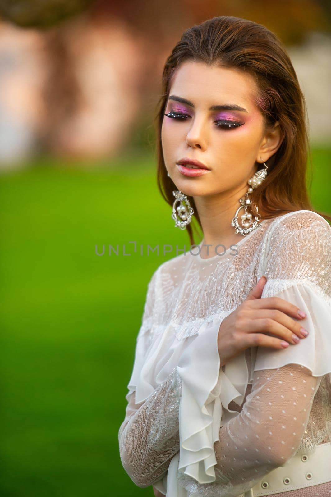 A bride in a white wedding dress in a park in an Austrian town with large trees at sunset.