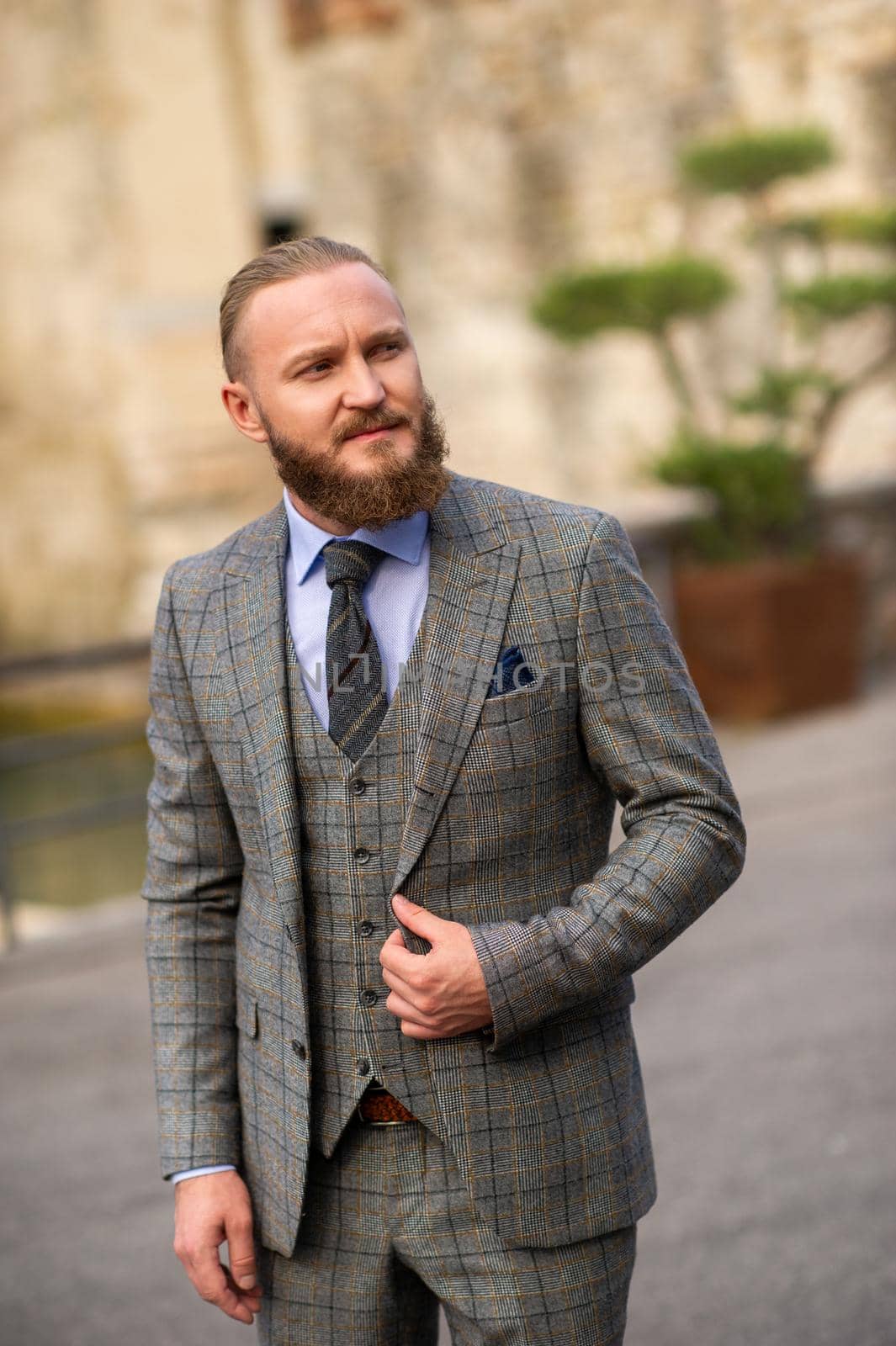 A man with a beard in a strict grey three-piece suit with a tie in the old town of Sirmione, a Stylish man in a grey suit in Italy.