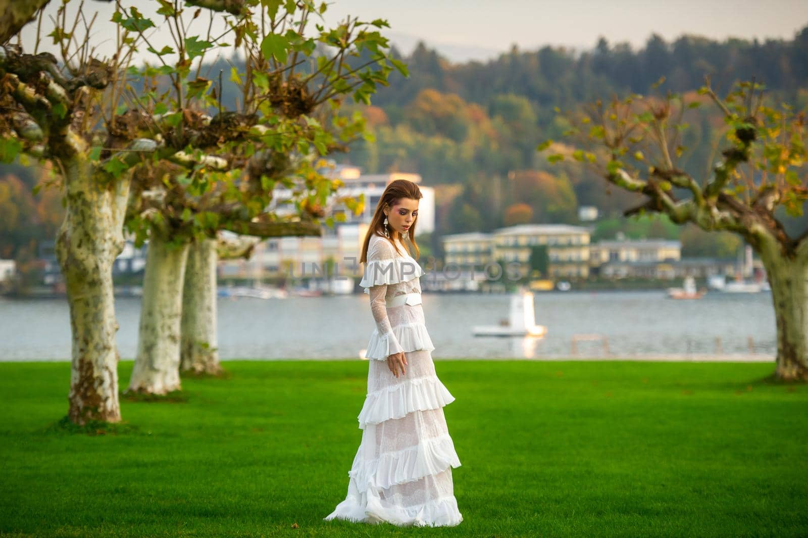 A bride in a white wedding dress in a park in an Austrian town with large trees at sunset.