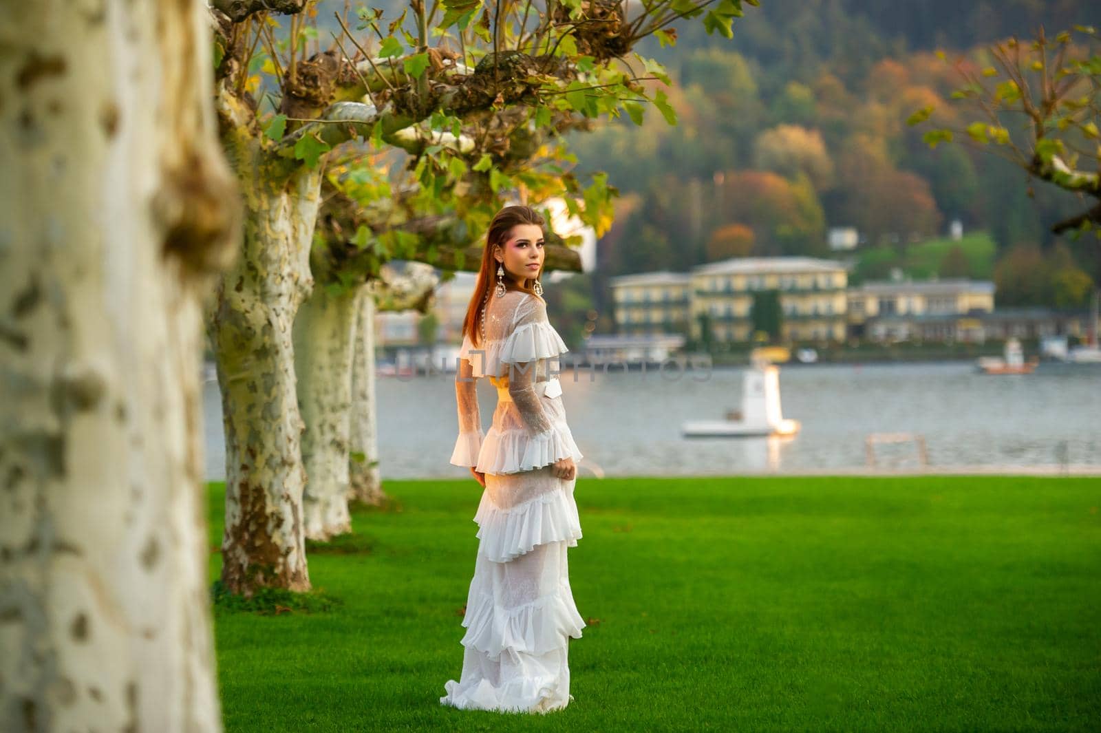 A bride in a white wedding dress in a park in an Austrian town with large trees at sunset by Lobachad