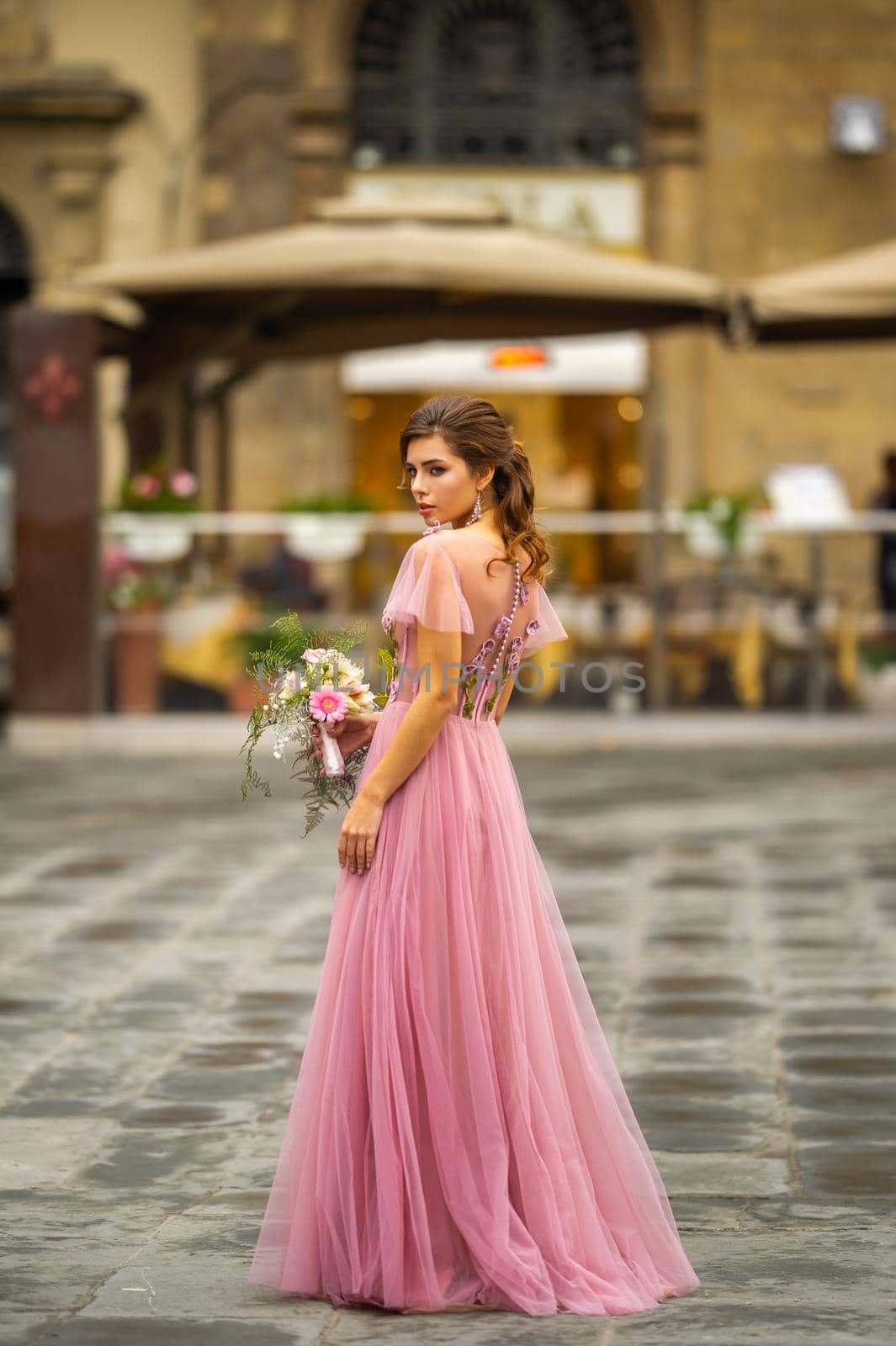 A bride in a pink dress with a bouquet stands in the center of the Old City of Florence in Italy by Lobachad