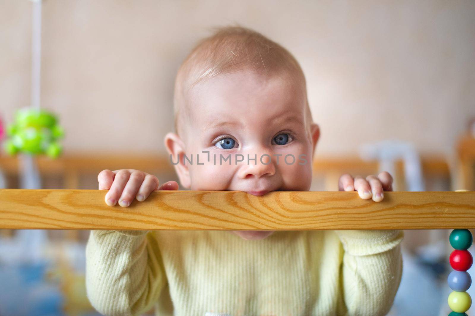 Closeup portrait of lonely toddler bites wooden bed frame. Child concept.