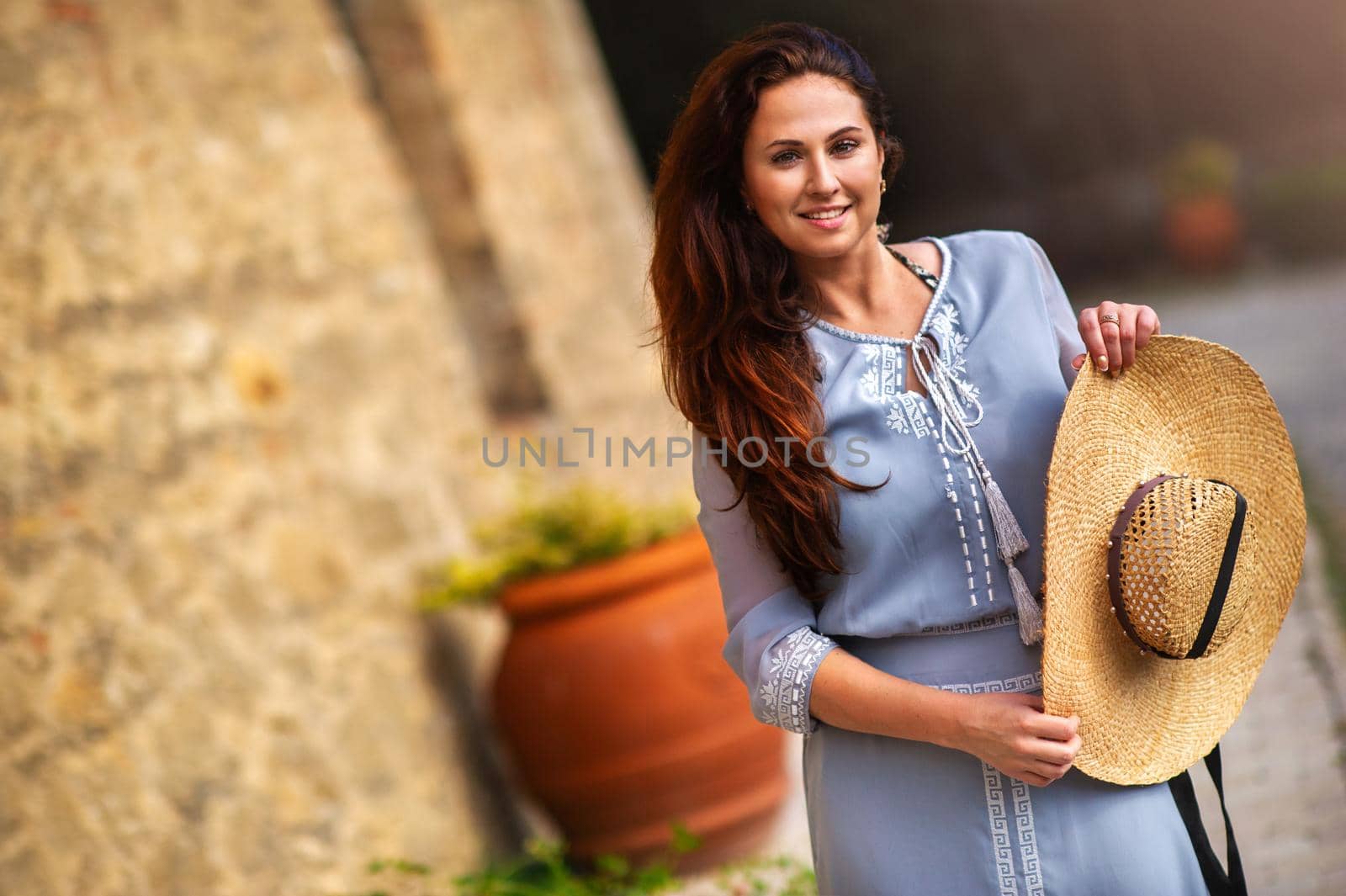 A girl in a dress and hat walks in the afternoon in an Italian town in Tuscany.