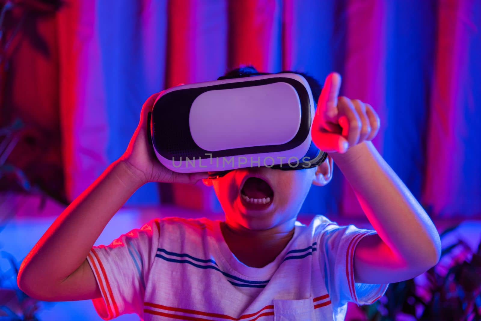 Asian little kid boy wearing virtual reality goggles experiencing reality, Child wear VR helmet excited open mouth at home dark purple and blue background, Virtual technology