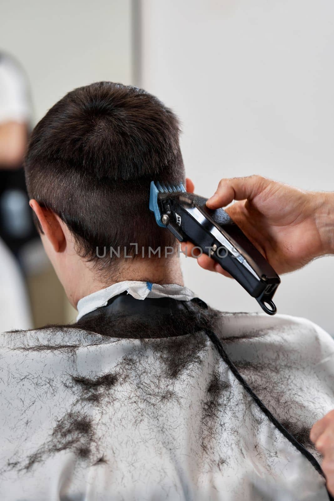 Barber cut hair with electric shearer machine on man in barber shop.