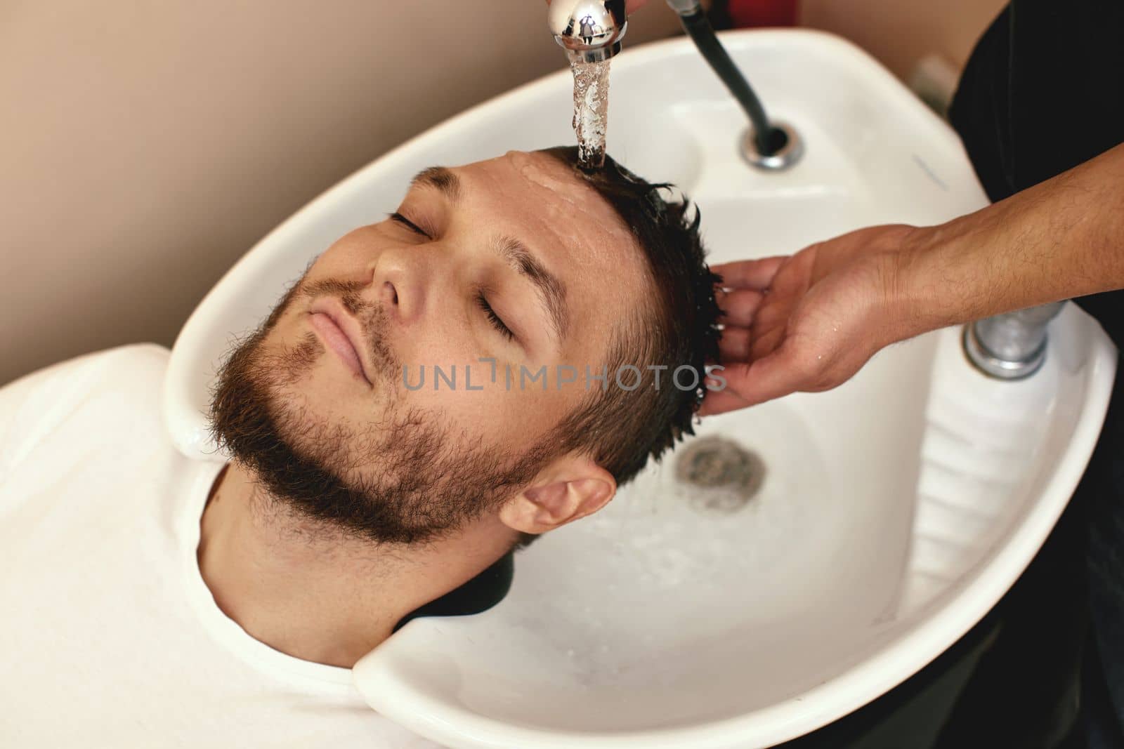 Barber washing hair of caucasian man in barber shop