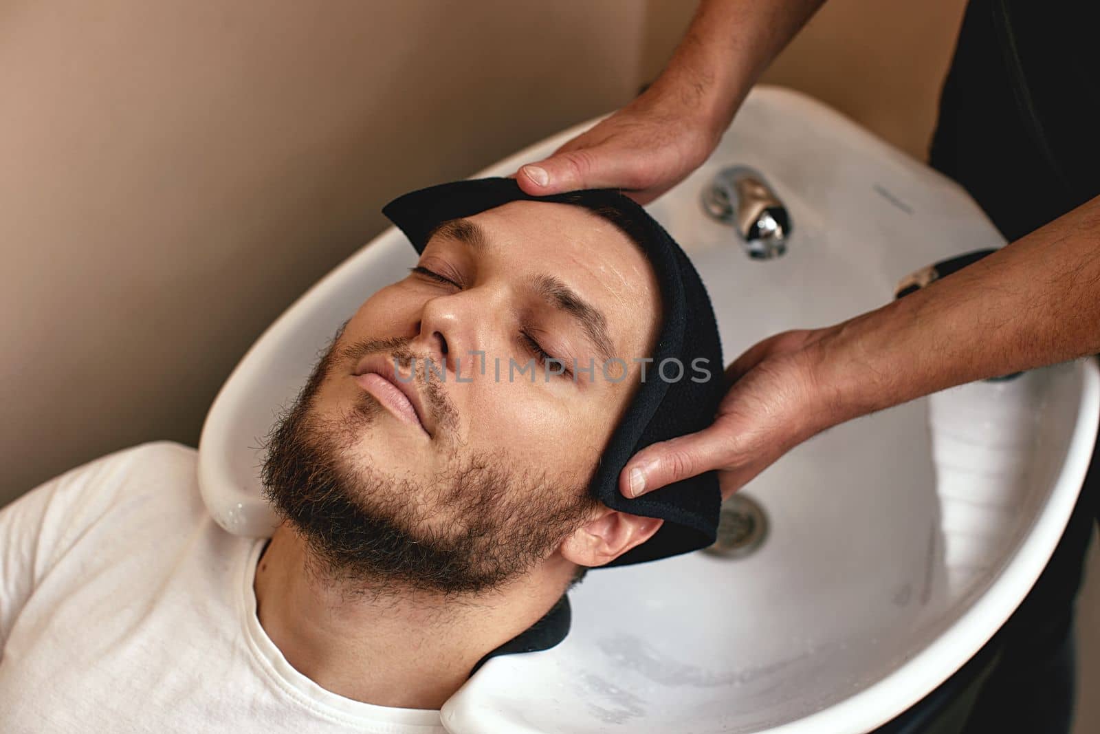 Barber washing hair of caucasian man in barber shop
