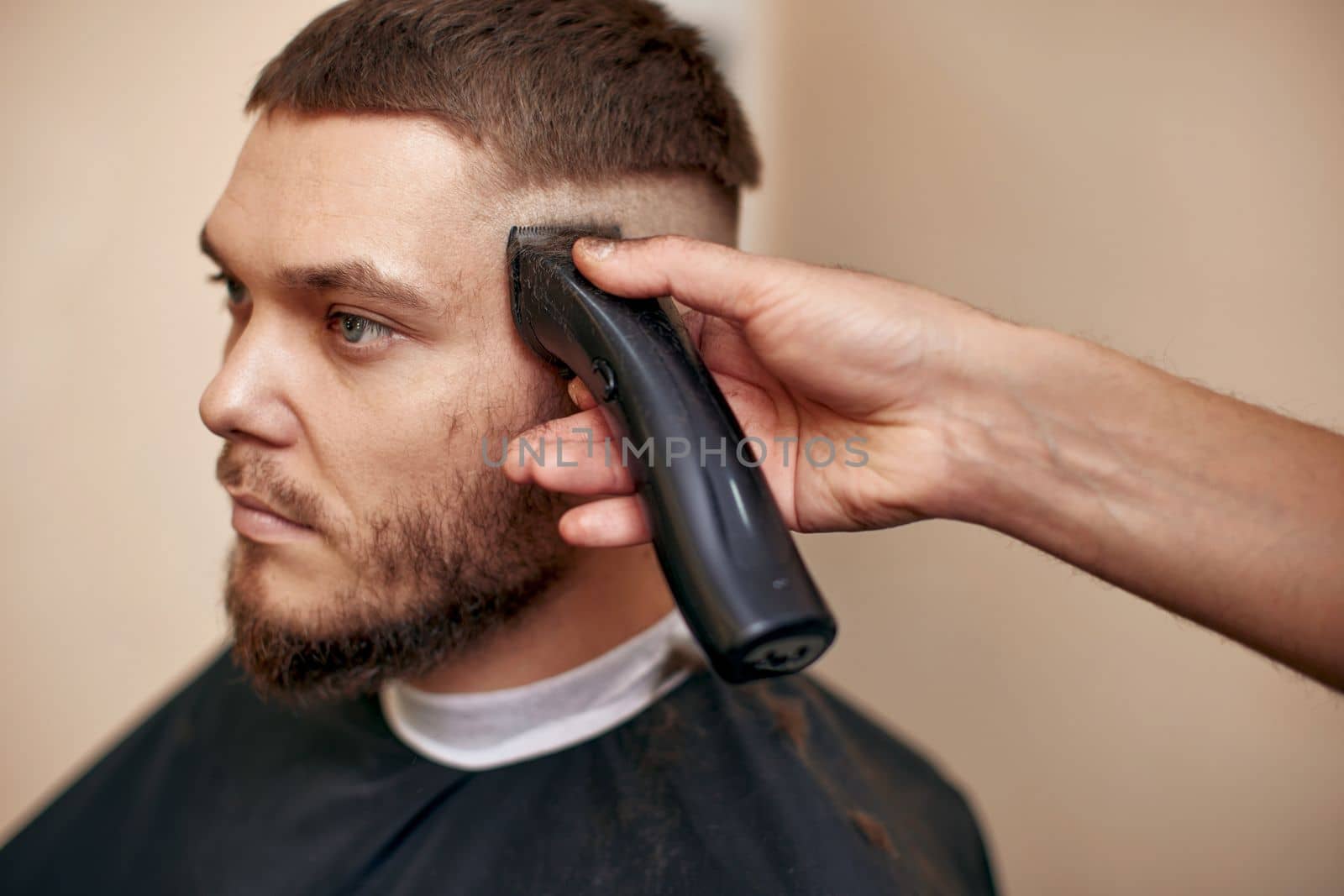 Barber trim hair with clipper on handsome bearded man in barber shop.