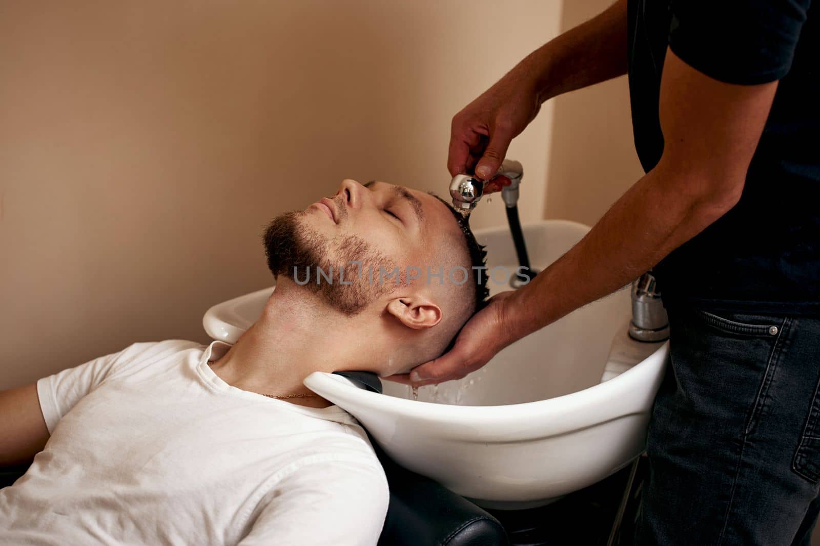 Barber washing hair of caucasian man in barber shop