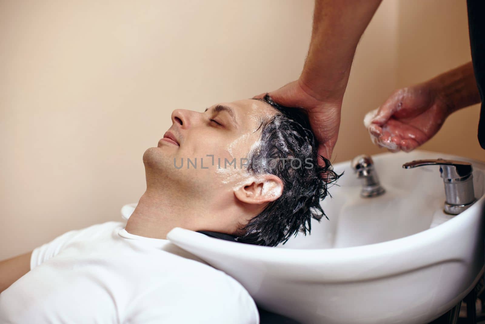 Barber washing hair of caucasian man in barber shop