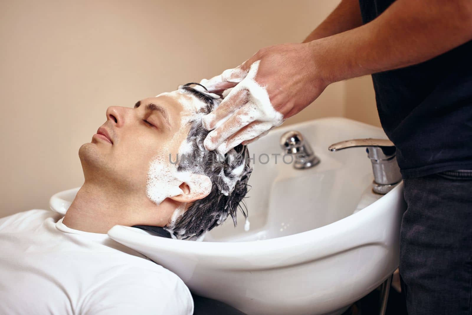 Barber washing hair of caucasian man in barber shop